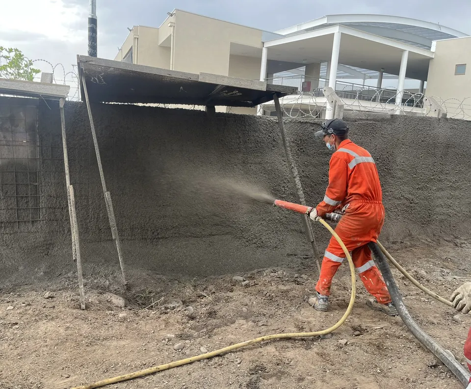 Operario con EPP proyectando shotcrete sobre un muro en obra